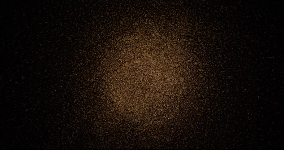An expanding sphere of gold glittering particles scattering on a dark background