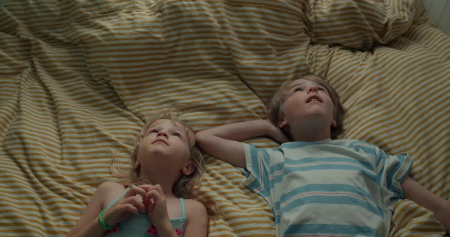 Brother and sister stare up toward the sky while laying on their backs on a blanket