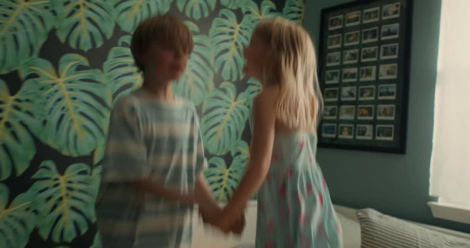 A brother and sister have lots of fun jumping up and down on a bed