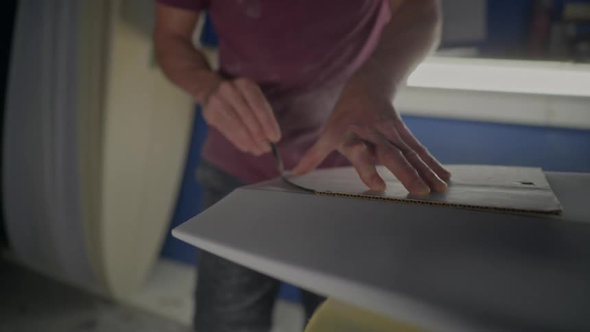 Close up of the hands of a person drawing with a stencil over a handmade surfboard