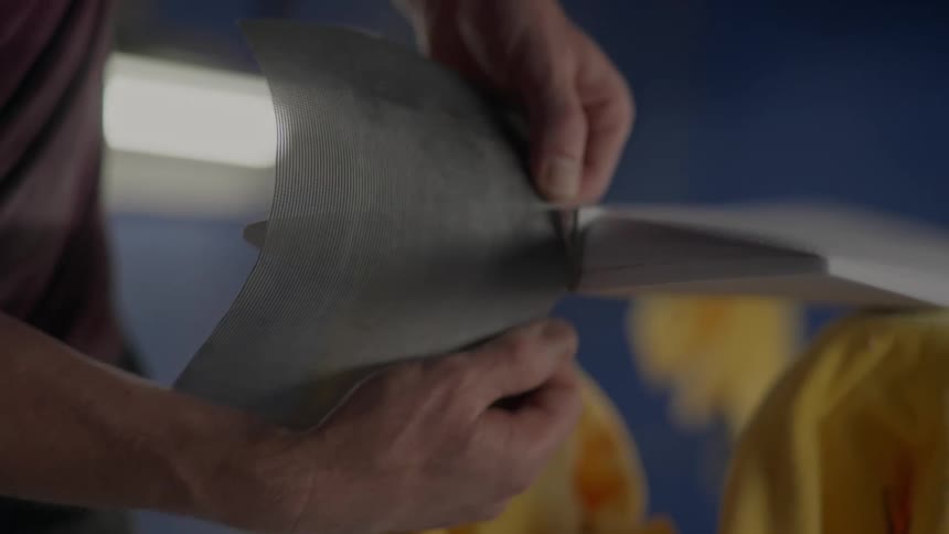 A closeup of a persons hands sanding the tail of a surfboard in a workshop