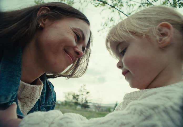 Little girl playing with her mothers denim blouse while they are in a field outdoors