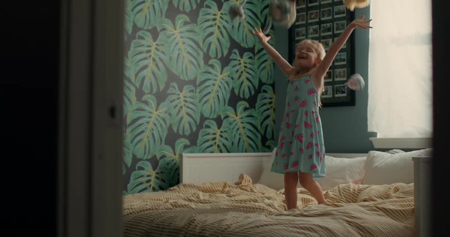 A child jumping in bed throwing plush toys in the air