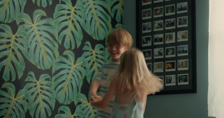 Brother and sister playfully jumping over a couch at home