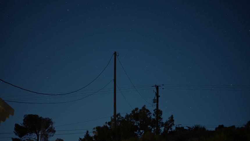 Starry night sky with silhouettes of electricity poles and wires against a dark background