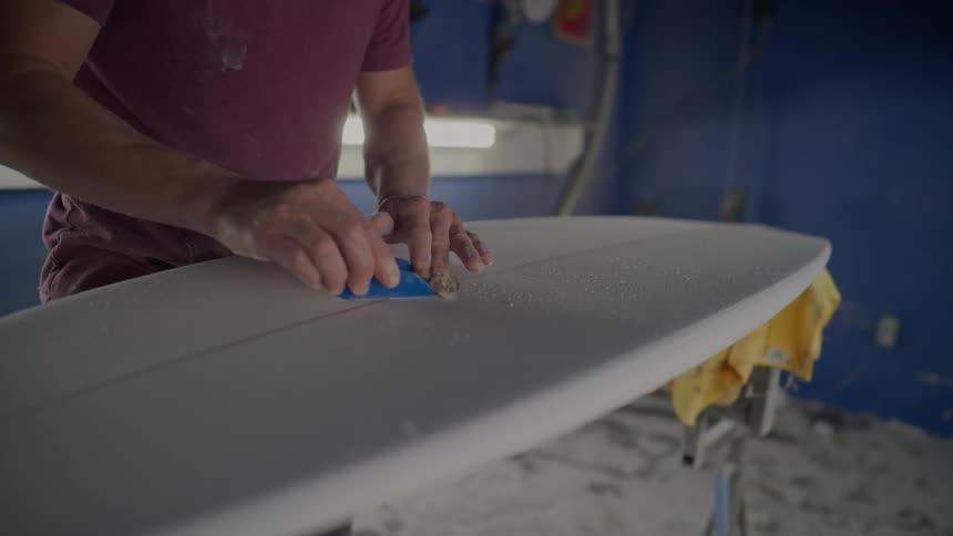 Person in a workshop working on finishing a white surfboard with a piece of sandpaper