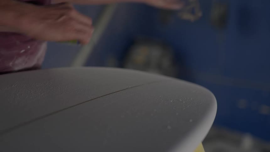 Person hands carefully working on a surfboard using a sanding tool to shape the surface