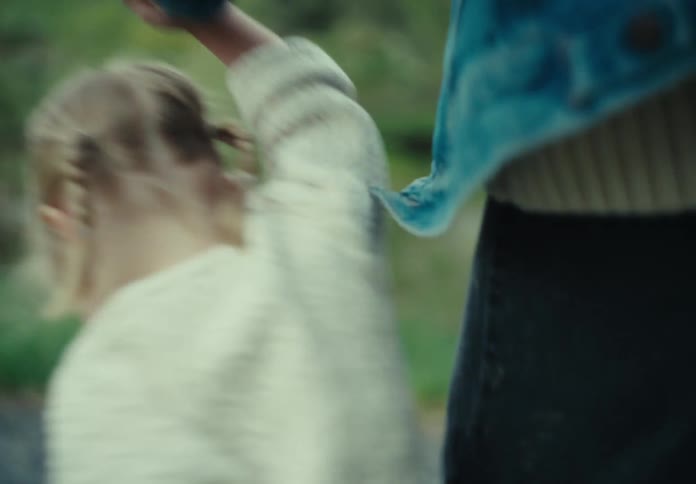 Daughter holds hands with a parent while walking on a path near a field