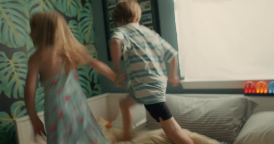 Brother and sister playfully jumping over a couch at home