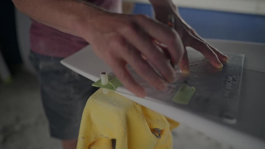 A man uses a measuring device to make marks on a surfboard