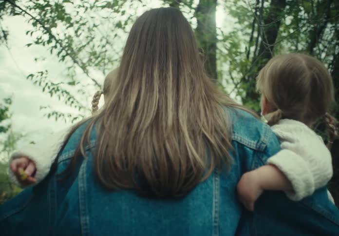 A mother carries her two daughters through a forested area
