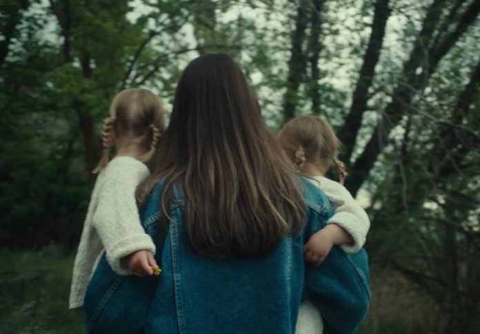 Mother carrying her two twin daughters on her lap in a natural environment with trees around