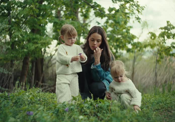 A mother picks wildflowers with her twin daughters on a summer day