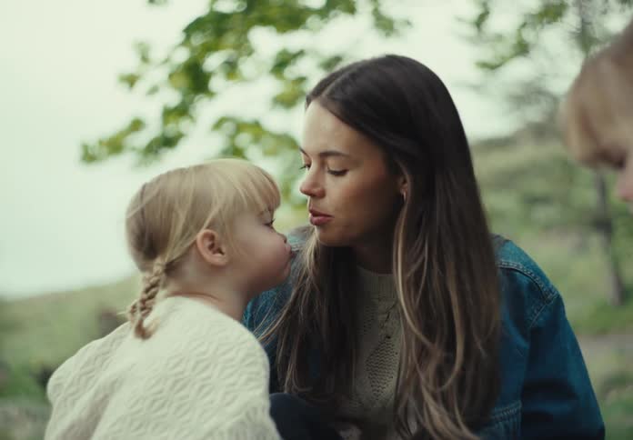 A mother and her daughters wearing thick lightcolored sweaters play around in the backyard