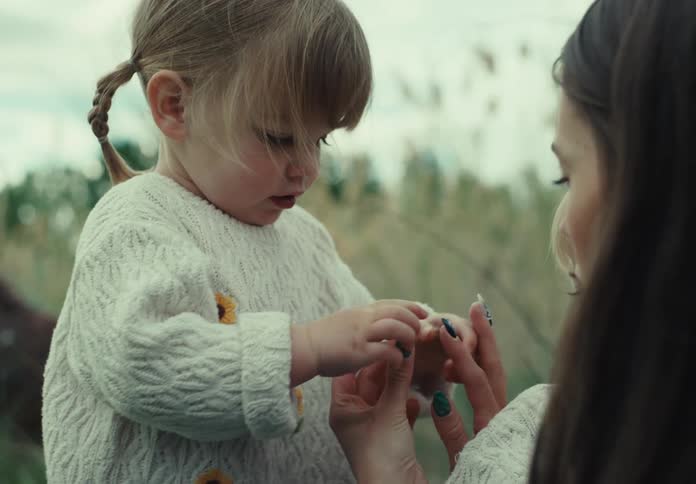 Mother holding a flower and giving it to her little daughter in front of her while they are in a field
