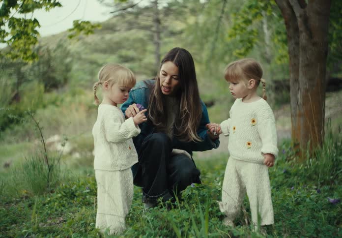 Mother crouching on a slope picks a flower that she hands to one of her two daughters