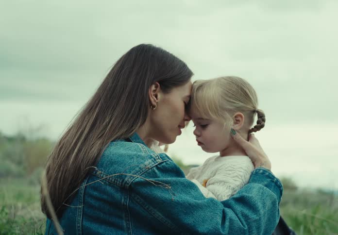 A mother sits outside while holding her daughters and talking to them