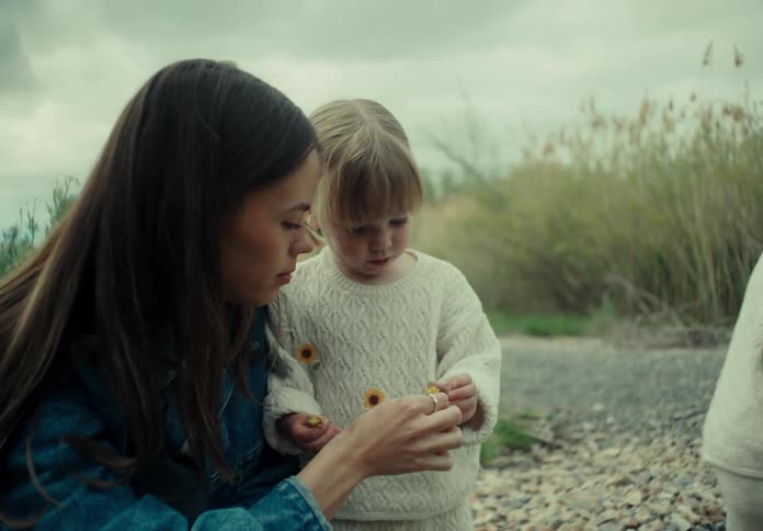 Mother in a field handing a flower into the hand of her little twin daughter