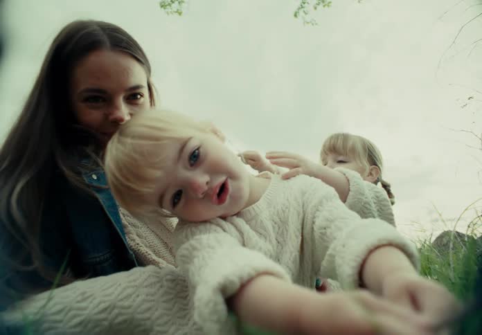 Mother sits in the grass with her daughters as they show things to her