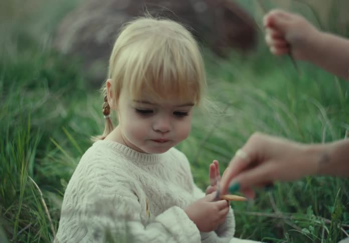 A girl wearing a knitwear sweater sitting on green grass plays with her sister