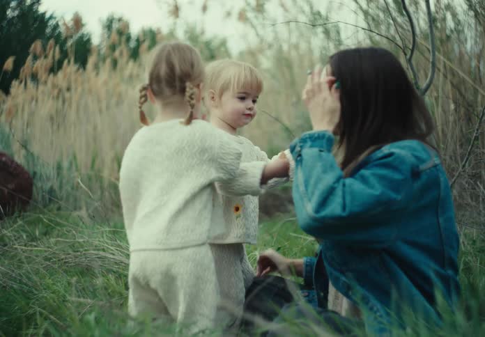 Mother sitting on the grass playing with her two young daughters and hugging one of them