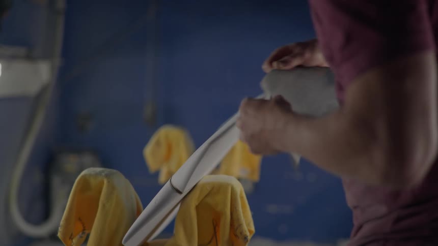 A closeup of a persons hands sanding the edge of a surfboard in a workshop