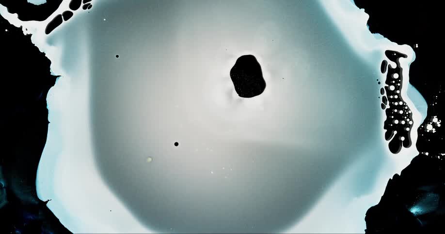 A large blob of white liquid expands and then contracts leaving behind much smaller blobs