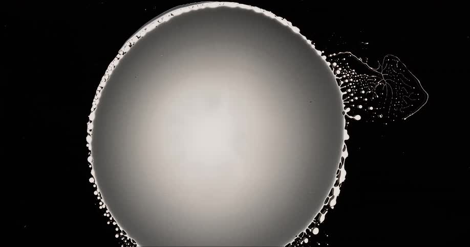 Large spherical fluid with a textured surface and a small cluster of particles against a dark background