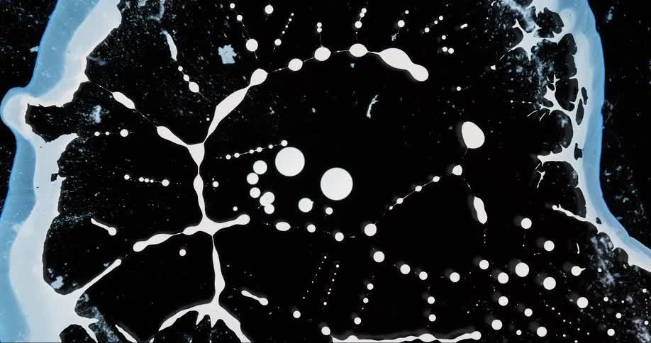 Closeup of a liquid substance dissipating beneath a dark surface