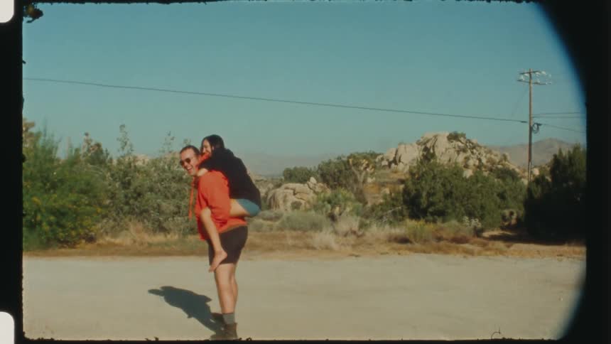 A woman riding on the back of a man who is walking on a road near the desert