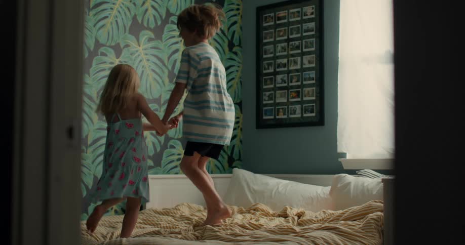 Young siblings laughing and holding hands jumping on the bed