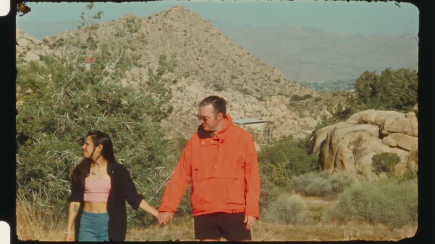 A man and a woman holding hands while standing on a road next to a desert