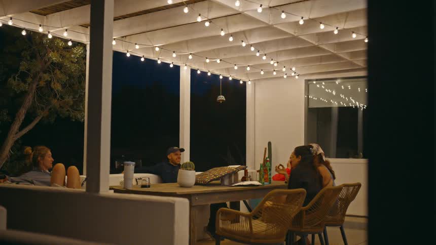 A group of friends sitting on an outdoor patio under string lights at night