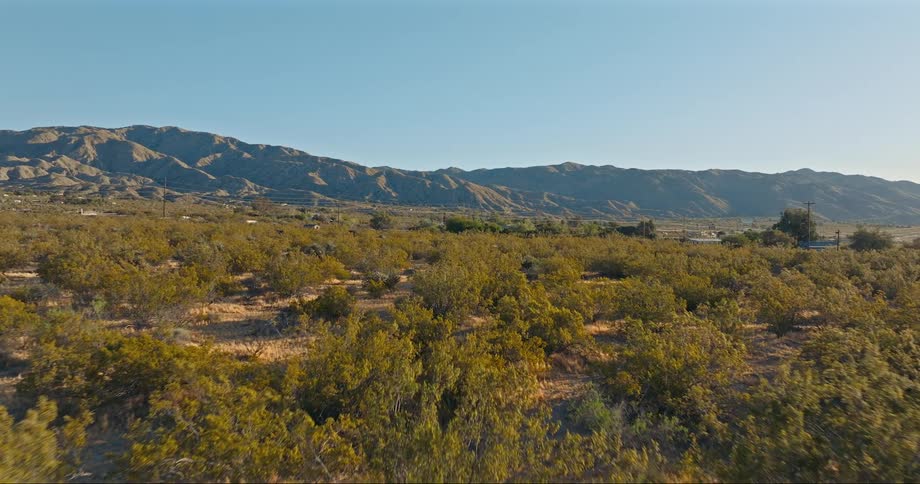 A road in a rural area carries vehicles past a desert and mountain range