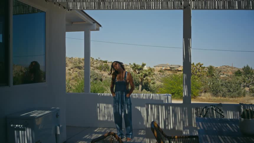 A woman stands on a deck and tilts her head back and forth