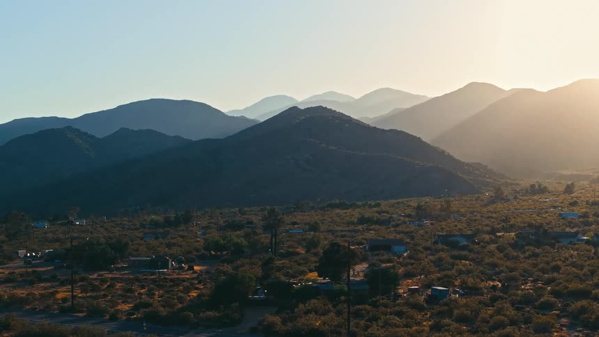 Landscape at dusk with mountains in the background and a residential area with sparse vegetation