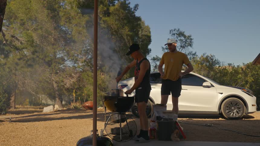 Two people outdoors one using a barbecue and the other standing next to it