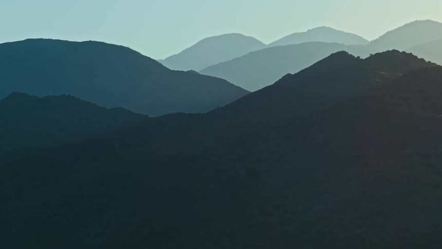 A hazy mountain range with overlapping ridges under a clear blue sky