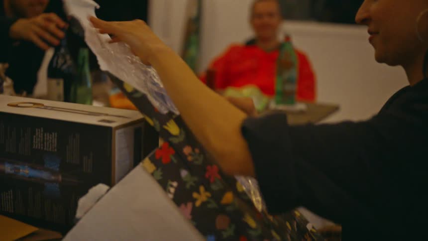 Woman sitting at a table with other people and opening a gift