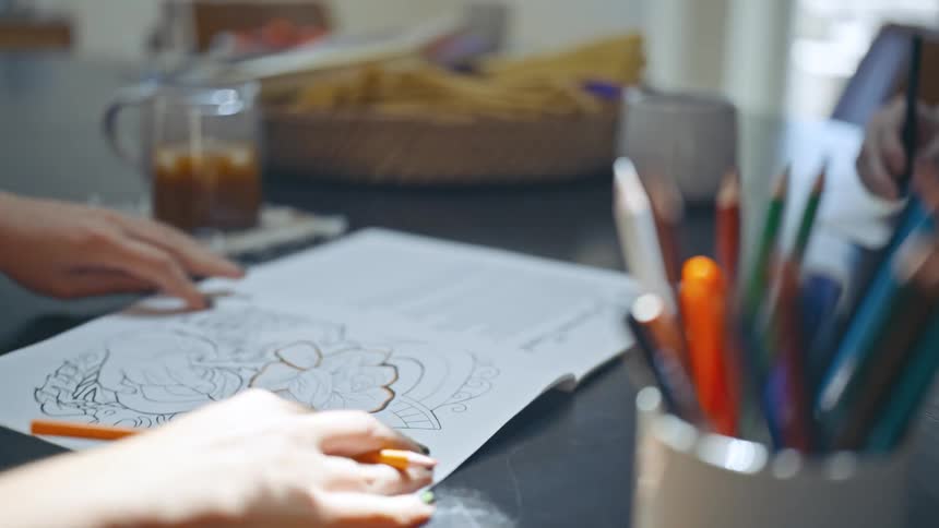 Two people draw and color while sitting at a table opposite each other