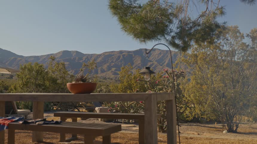 Smoke wafts into a yard next to a forest and mountains in a rural area