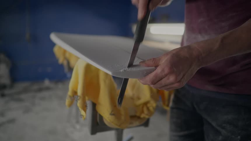 Pair of a mans hands cutting the bottom of the surfboard