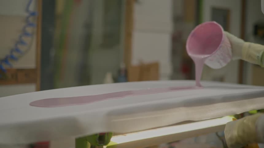 A man pours paint on a board in the shop