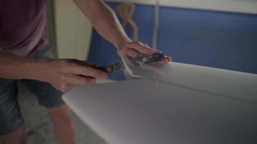 A man gently and carefully cuts through part of a surfboard