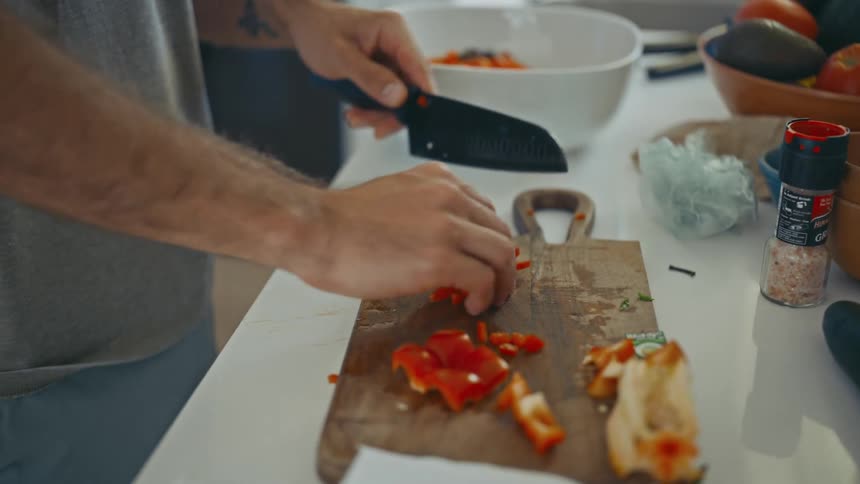A human hand cutting vegetables using a black knife on a wooden board