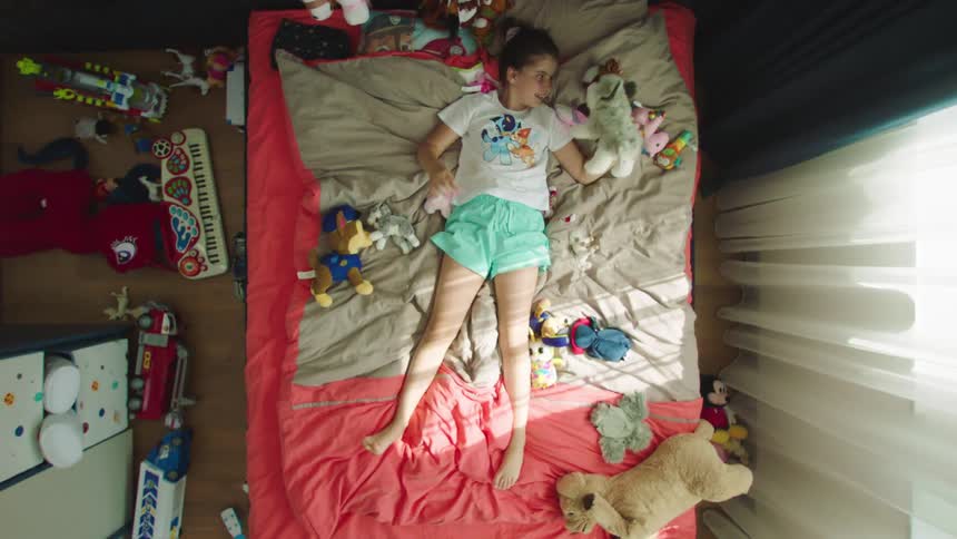 Little girl lying on the bed with several teddy bears and toys