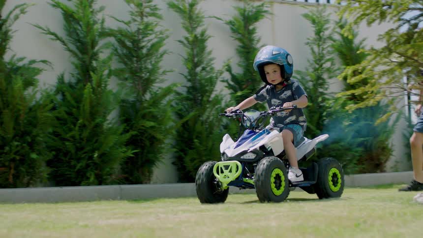 Three small boys running and playing in the backyard of a house with one of them riding an atv