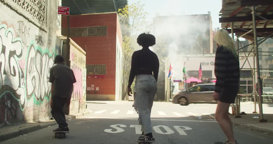 Three people skateboard to an intersection in a city