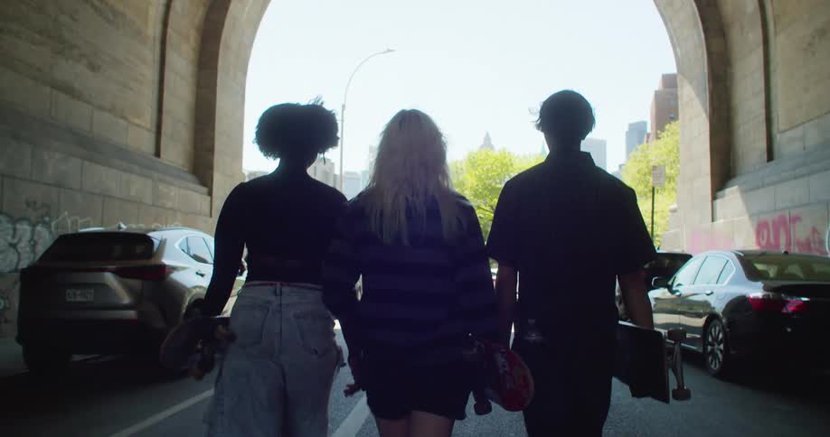 Three young friends holding skateboards in their hands and walking down a covered city street