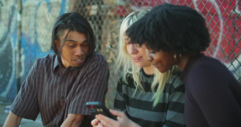 Three friends in the city and laughing and talking about something they see on a smartphone